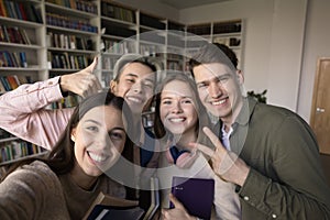 Multiethnic students standing together in library pose for smartphone camera