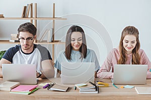 multiethnic students using laptops while sitting at table