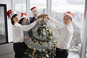 Multiethnic team of people putting christmas tree decor in festive office