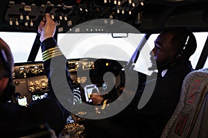 Multiethnic team of pilots using control panel in cockpit to fly airplane