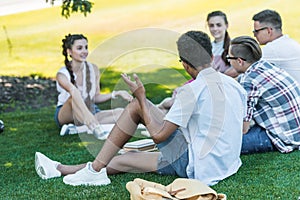 multiethnic teenage students sitting on grass and studying together