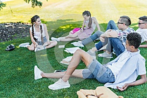 multiethnic teenage students sitting on grass talking and studying