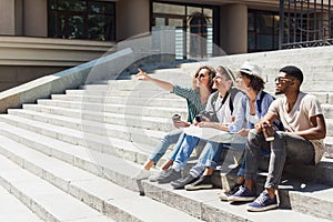 Multiethnic tourists sitting on stairs with map
