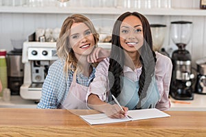 Multiethnic waitresses smiling and writing an order at cafe