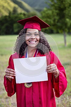 Multiethnic woman in her graduation cap and gown holding a sign or certificate