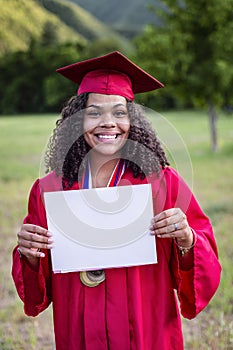 Multiethnic woman in her graduation cap and gown holding a sign or certificate photo