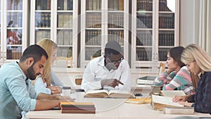 Multiethnic young people sitting at table reading reference books for study notes. Group of young students doing school