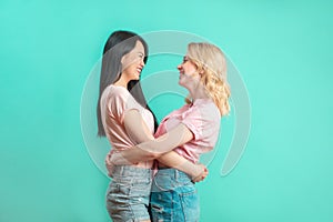 Multiethnic young women hugging at blue studio background with copy space