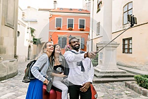 Multiethnical happy young people, African guy and two Caucasian girls, making selfie photo with funny laughing faces