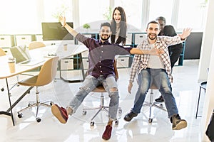 Multiethnics startup business team of software developers having fun while racing on office chairs,excited diverse employees