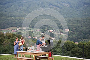 Multigeneration family with wine outdoors on garden barbecue, grilling.