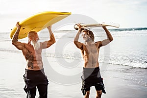 Multigeneration friends going to surf on tropical beach - Family people having fun doing extreme sport - Joyful elderly and