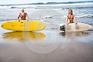 Multigeneration friends going to surf on tropical beach - Family people having fun doing extreme sport - Joyful elderly and