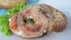 Multigrain bagel with cream cheese, salmon slices, dill and salad. Adding spices, slow motion.