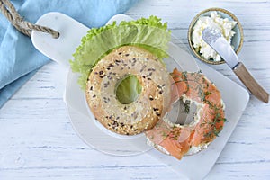 Multigrain bagel with cream cheese, salmon slices, dill and salad, top view