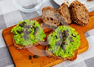 Multigrain toasts with guacamole and pumpkin seeds on wooden board