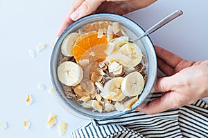 Multigrain wholewheat breakfast cereals with tangerine, coconut chips, peanut butter and banana, top view