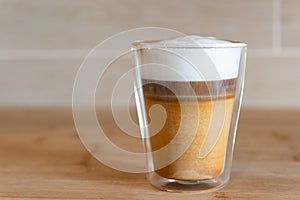 Multilayer coffee or cappuccino in a glass cup on wooden table