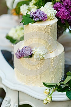 The multilevel wedding cake with lilac flowers on the table