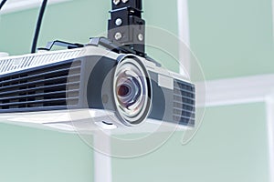 Multimedia projector hanging on the ceiling of modern conference room. Monochrome indoors picture.