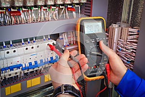 Multimeter is in hands of electrician on background of electrical automation cabinet.