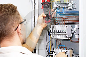 Multimeter is in hands of electrician on background of electrical automation cabinet. An electrician is checking the voltage in an