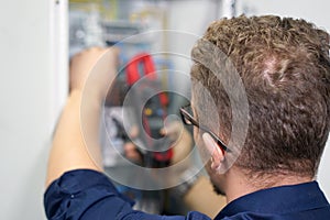 Multimeter is in hands of electrician on background of electrical automation cabinet. An electrician is checking the voltage in