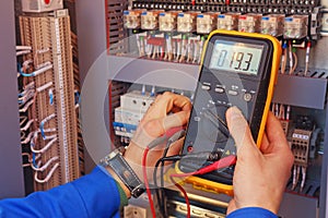 Multimeter in the hands of an electrician close-up on a blurred background of electrical elements