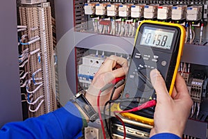 Multimeter in hands of electrician engineer in electrical cabinet. Maintenance of electric system photo