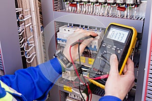 Multimeter is in hands of engineer in electrical cabinet. Adjustment of automated control system for industrial equipment photo