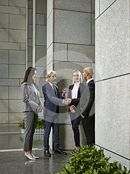 Multinational businesspeople meeting shaking hands in lobby of modern office building