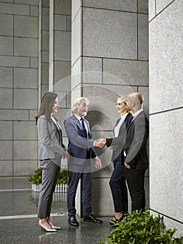 Multinational business people meeting shaking hands in lobby of modern office building