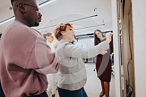 Multinational colleagues collaborate in a classroom, sharing ideas and discussing statistics on a whiteboard, aiming for