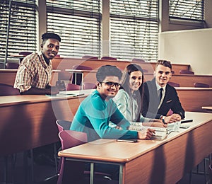 Multinational group of cheerful students taking an active part in a lesson while sitting in a lecture Hall.