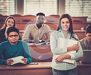 Multinational group of cheerful students taking an active part in a lesson while sitting in a lecture hall.