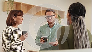 Multinational group of ethnically diverse young man and women relaxing while having coffee break at work in light modern