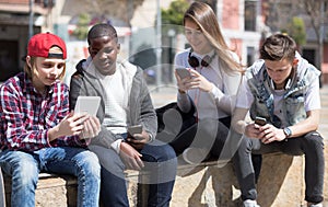 Multinational teenagers play in smartphones in schoolyard