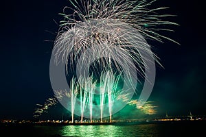 Multiple colorful fireworks burst in the night sky with light trails over the sea