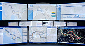 Multiple computer screens displaying maps and data visualizations in a control center