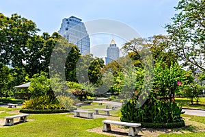 Multiple empty benches in Lumpini city park, view at Bangkok skyscrapers