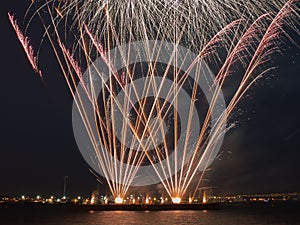 Multiple fireworks burst in the night sky with light trails
