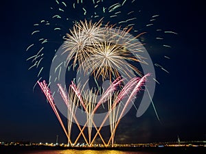 Multiple fireworks burst in the night sky with light trails and golden circles of fireworks