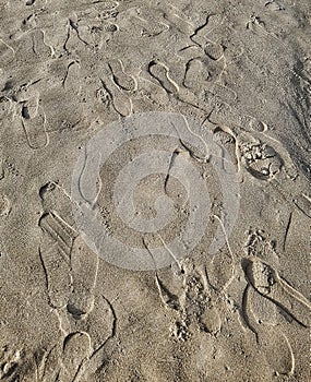 Multiple footprints in sand at the beach on a sunny day. Foot imprints background, shoe marks