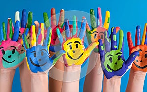 Multiple hands painted in various colors, each with a smiling face, raised against a blue background. The hands are positioned in