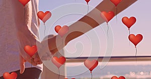 Multiple heart balloons floating against mid section of couple holding hands at beach