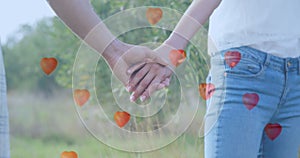 Multiple heart balloons floating against mid section of couple holding hands in the garden