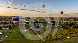 Multiple Hot Air Balloons Soar Over A Picturesque Landscape Featuring A Corn Maze, At Golden Sunset.