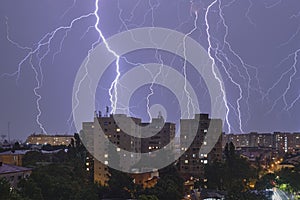 Multiple lightning strikes and thunderstorm over city buildings, at night. Weather phenomena
