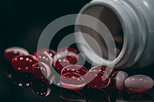 Multiple red and white pills spilled from bottle on black background