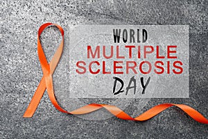 Multiple Sclerosis Awareness Day. Orange ribbon on grey background, top view